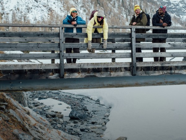 Vier Freunde genießen die Aussicht von einer Holzbrücke aus, in einer verschneiten Landschaft