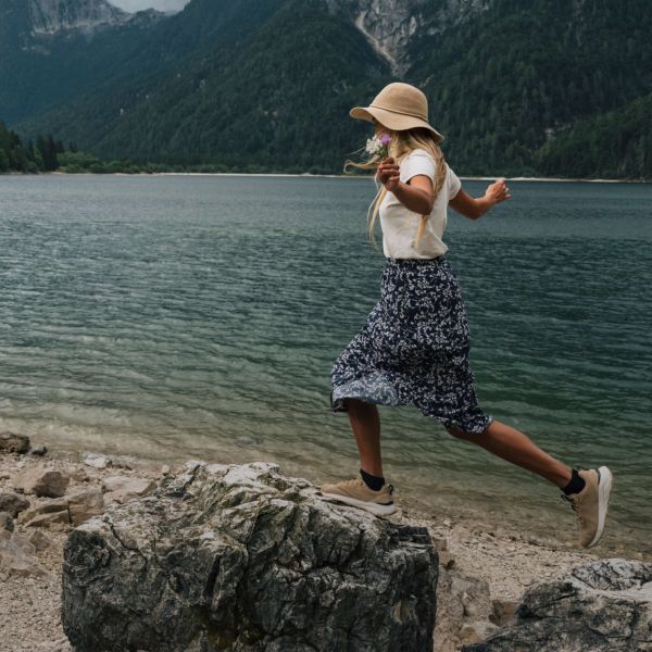 Una donna in abbigliamento outdoor estivo sta in equilibrio su una roccia in riva a un lago