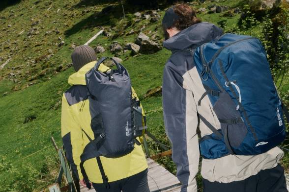 Foto da dietro di due escursionisti con zaini sulla schiena che attraversano un ponte di legno