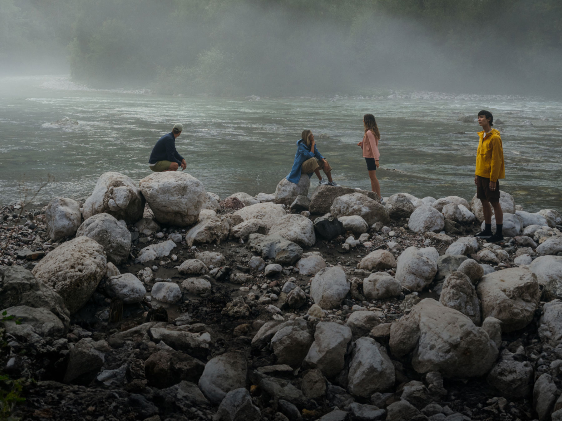 Paesaggio nebbioso con 4 persone su rocce davanti a un fiume
